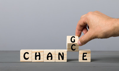 Hand flip wooden cube with word "change" to "chance" on grey background