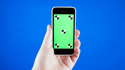 Close up. A man's hand holds a smartphone with a green screen. Blue screen background and the tracking markers.