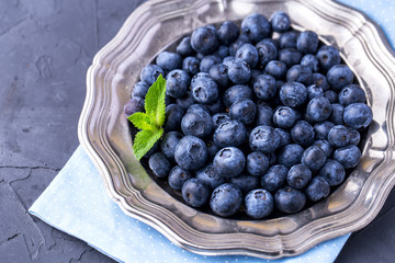 ripe, large blueberries in metal plate, on blue textile napkin, with mint leaf, top view