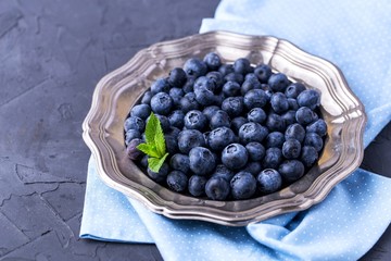 ripe, large blueberries in metal plate, on blue textile napkin, with mint leaf, top view