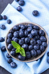 ripe, large blueberries in metal plate, on blue textile napkin, with mint leaf, top view