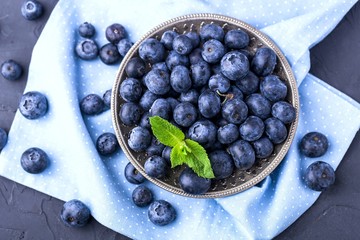 ripe, large blueberries in metal plate, on blue textile napkin, with mint leaf, top view