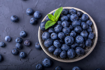 ripe, large blueberries in a metal plate, with a leaf of mint, on a dark gray stone table, top view