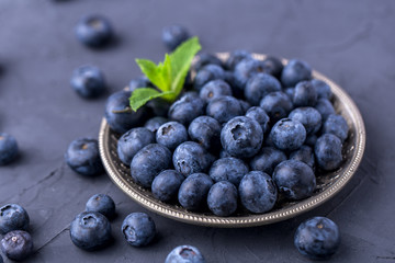 ripe, large blueberries in a metal plate, with a leaf of mint, on a dark gray stone table, top view