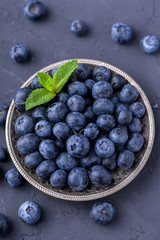 ripe, large blueberries in a metal plate, with a leaf of mint, on a dark gray stone table, top view