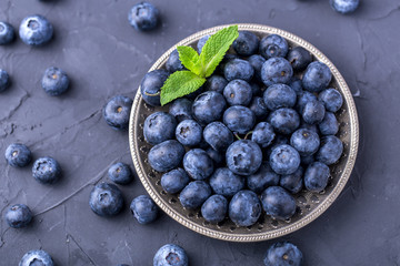 ripe, large blueberries in a metal plate, with a leaf of mint, on a dark gray stone table, top view