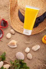 Sun lotion SPF cream bottle, summer straw hat and sunglasses on sand beach. Flat lay