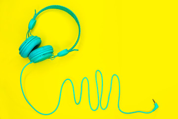 Blue headphones lie on a colorful yellow background with copy space.