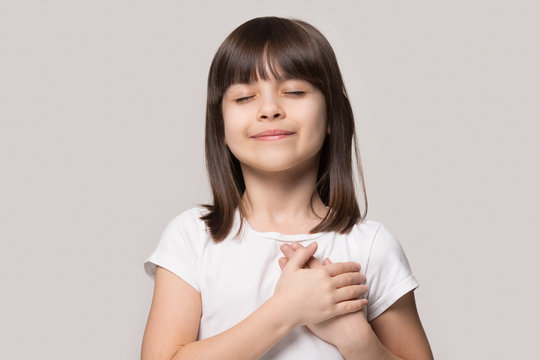 Little girl closed eyes hold hand on chest feels gratitude