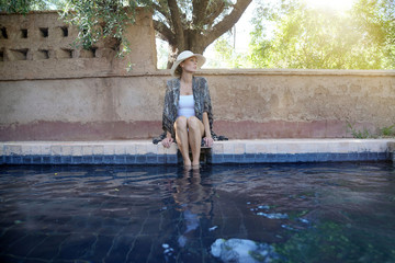 Stunning woman siting by Moroccan swimming pool