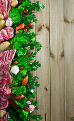 Wooden background with raw lamb, vegetables, greens