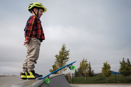 A young boy stands at the edge of a half pipe ramp at a skateboard park.