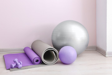 Set of sports equipment with fitness ball near light wall