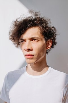 Curly man posing by white background in contrast daylight