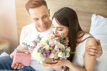 Husband greeting his wife with bouquet of flowers in bedroom at home