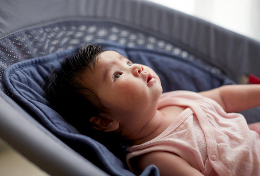 Cute Asian baby, sitting on a small lounger and playing with himself,  at home