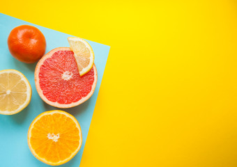 Flat lay of cut ripe juicy grapefruit, lemon and orange on yellow and blue background. Citrus pattern.