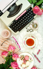 Romantic vintage feminine writing scene, tea break with old typewriter and pink roses on marble table top down overhead.