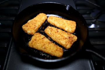 Breaded fish sticks baked in a cast iron skillet, resting on the stove.