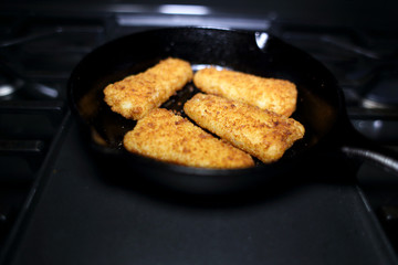 Breaded fish sticks baked in a cast iron skillet, resting on the stove.