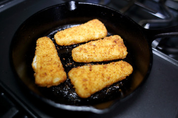 Breaded fish sticks baked in a cast iron skillet, resting on the stove.
