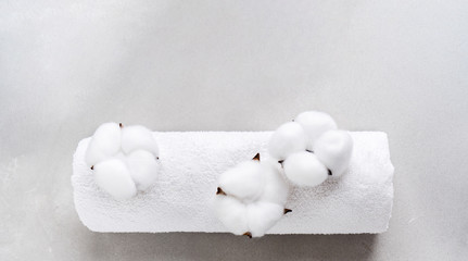 White fluffy towel twisted into roll with flowers of natural cotton on gray background with copy space. Spa concept. Flat lay.