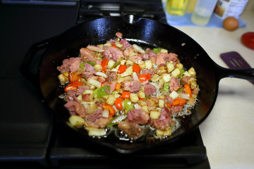 Corned beef hash frying in a cast iron skillet on a natural gas stove top in a home kitchen.