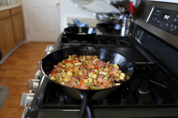 Corned beef hash frying in a cast iron skillet on a natural gas stove top in a home kitchen.