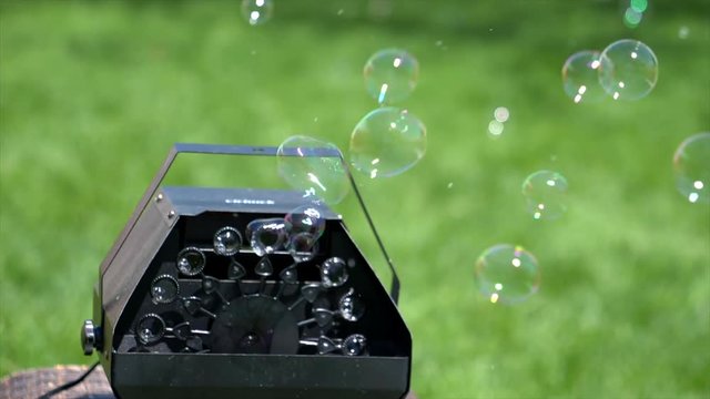 Bubbles are seen blowing automatically out of a black bubble machine.  A grassy lawn is seen in the background.