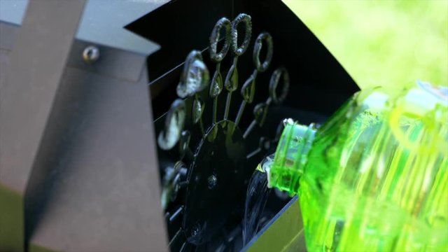 A container of bubbles is seen being poured into a black automatic bubble machine.  Bubbles are blowing continuously.