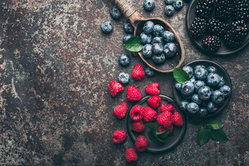 Fresh berries with raspberries, blueberries, blackberries in bowl on a stone stand on a dark metal background.
