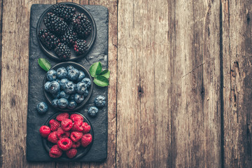 Fresh berries with raspberries, blueberries, blackberries in bowl on a stone stand on wood background.