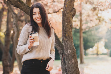 Beautiful woman drink coffee and posing for the camera in autumn park.