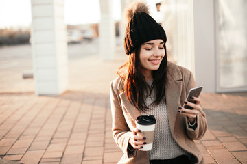 Happy smiling woman using phone and drink coffee sitting on the street.