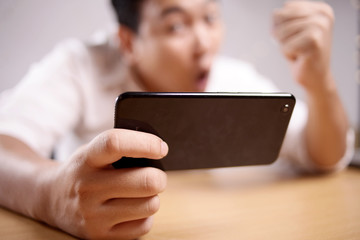 Funny Young Asian Guy Playing Games on Tablet Smart Phone