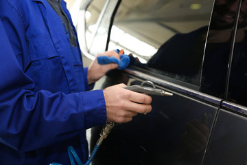 Worker cleaning automobile with gun and rag at car wash, closeup