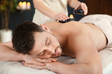 Fototapeta na wymiar Handsome man receiving hot stone massage in spa salon