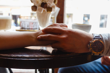 Young girl and young man holding hands on wooden table in cafe. A man and a woman holding hands in a cafe restaurant, a young couple enjoying a cozy cafe and each other, close-up