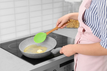 Woman stirring butter in frying pan on electric stove, closeup