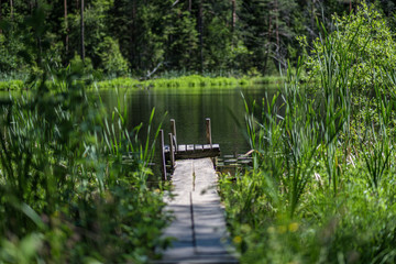 nice wooden plank boardwalk leans into blue lake with green shores and blue sky