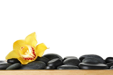 Wooden tray with spa stones and orchid flower against white background