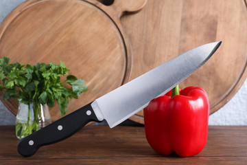 Chef knife, bell pepper and serving boards on wooden table against grey background. Clean dishes
