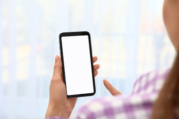 Woman holding smartphone with blank screen on blurred background, closeup of hands. Space for text