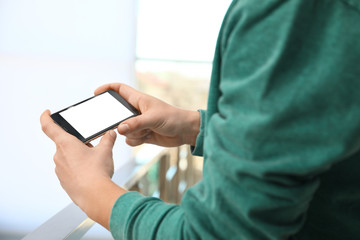 Man holding smartphone with blank screen indoors, closeup of hands. Space for text