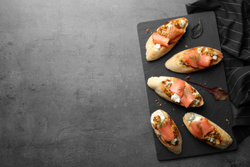 Slate plate with tasty bruschettas on grey table. Space for text