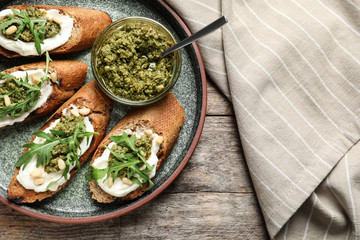 Plate with tasty bruschettas and pesto sauce on wooden table, top view. Space for text