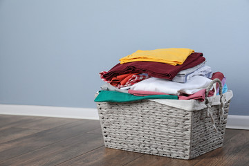 Wicker laundry basket with clean clothes on floor near color wall. Space for text