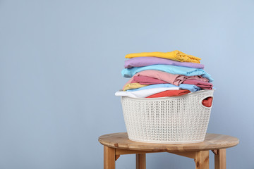 Plastic laundry basket with clean clothes on stool against color background. Space for text