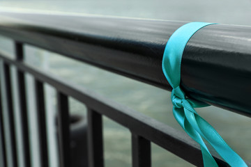 Teal ribbon tied to railing outdoors, space for text