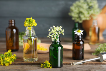 Bottles of essential oils, pipette and flowers on wooden table